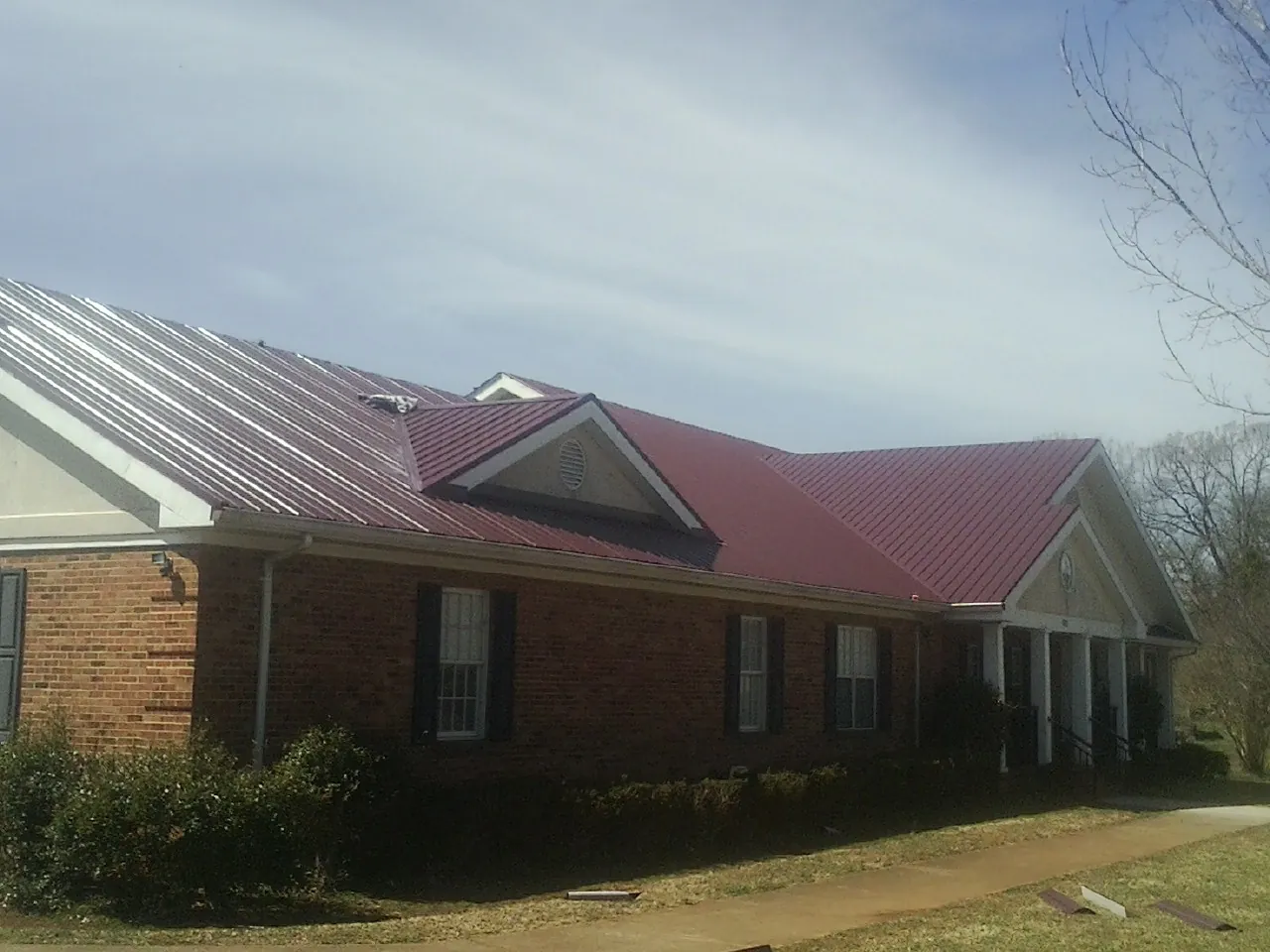Red metal roof with gabled entries on a long brick building, from a Hail Damage Roof Repair job in Rockport