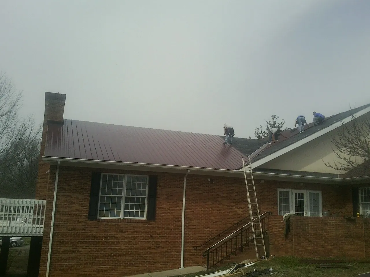 Crew setting red metal roofing panels on a brick home in Rockport