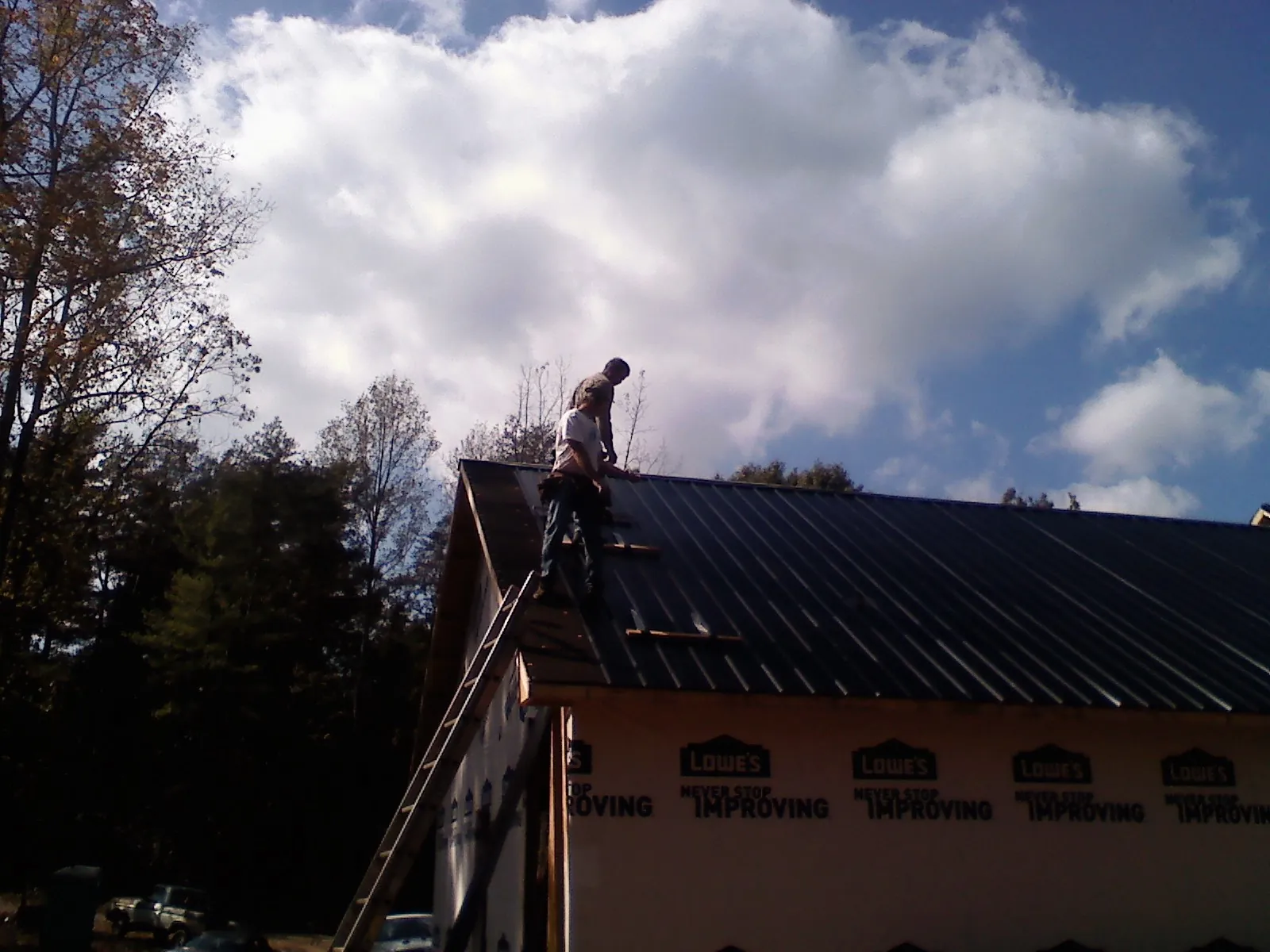 Roofer fastening dark metal panels high against a cloudy sky, from a Roof Inspection job in Rockport