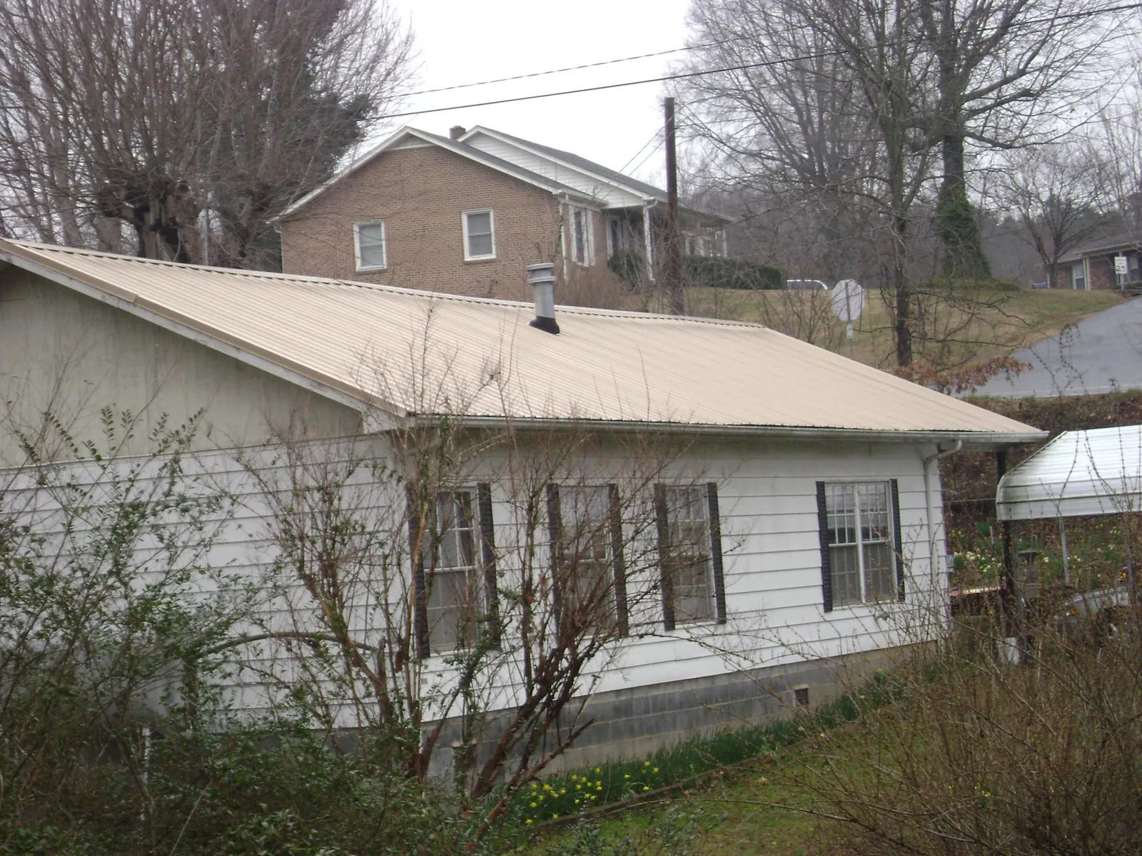 Tan metal roof on a white sided house set into a hillside — Commercial Roofing by Roofing Brothers in Rockport